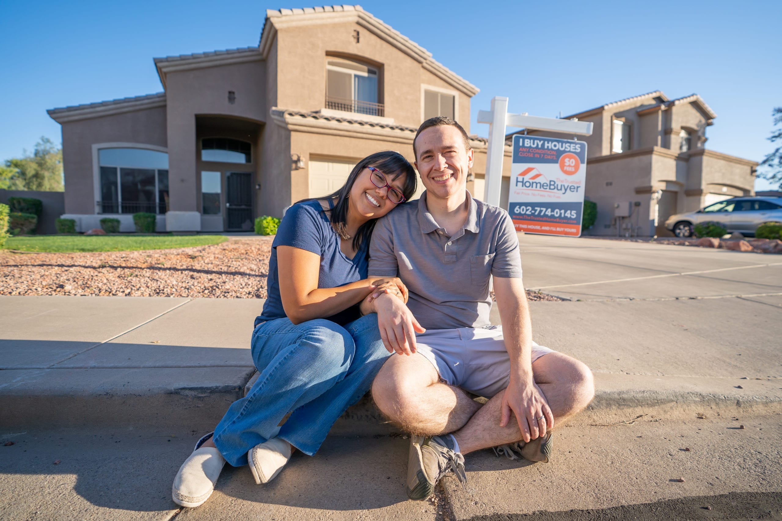 a man and woman sitting on a curb with a building in the background