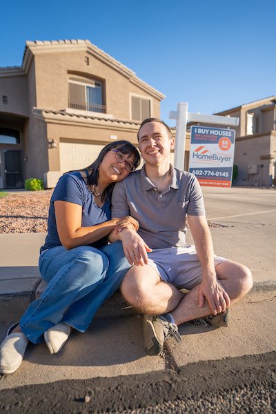 Young couple happily sitting on curb in front of a house that they just bought in Phoenix Arizona