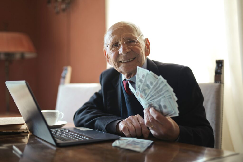 a happy senior businessman holding a money while working on laptop placed at the table